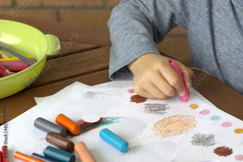Close-up shot of little child coloring picture crown illustration with crayon, felt-tip pens, pencils of different colors on wooden table. Child smiling face happy colouring. coronation day. 