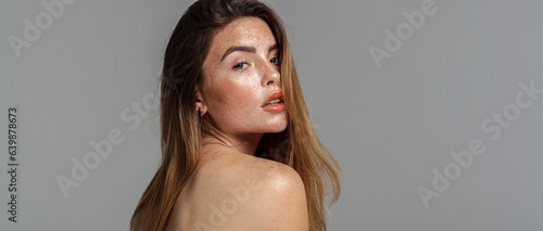 Studio beauty portrait of very natural woman with freckles on her face and shoulder. Girl looking at the camera.