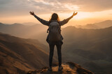 Back view of woman raises his hands up while standing on top of the mountain at sunset a hike in summer