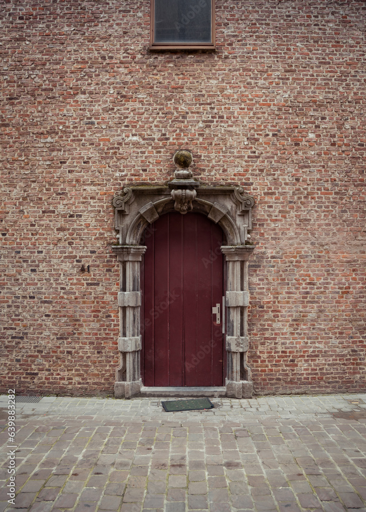 Brick wall with maroon-brown door. Old stone house wall with a baroque-styled door portal on side street in Brussels. 