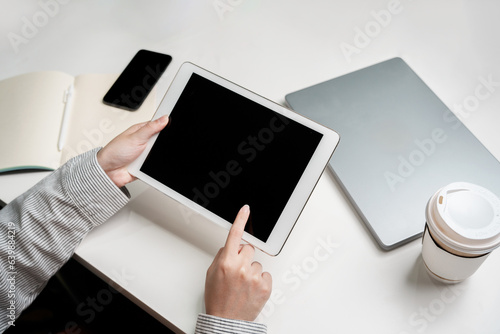 Finger pointing on black screen touch pad screen for mockup multimedia technology device with tablet phone and coffee on table indoor workspace working on reviewing and reading application document