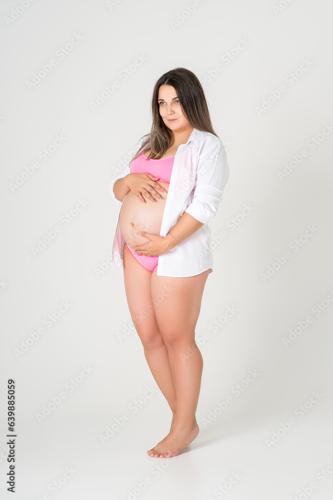 Fototapeta premium Plus size pregnant woman in pink underwear on gray background, maternity clothes, pregnancy concept