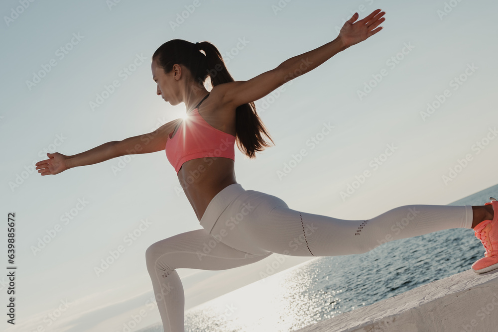 Attractive young woman in sportswear stretching out hands while exercising seaside Attractive young woman in sportswear stretching out hands while exercising seaside