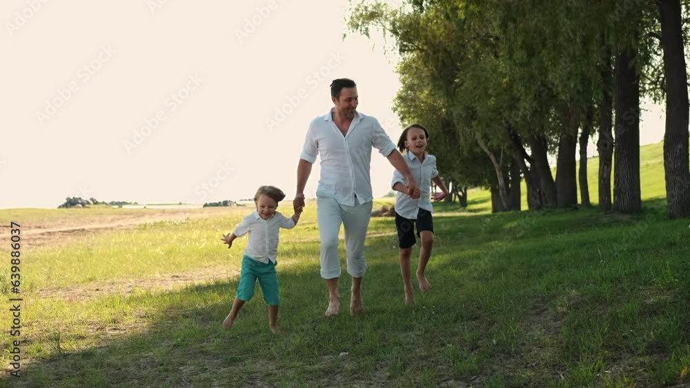 Father and two sons run through the grass holding hands Father and two sons run through the grass holding hands