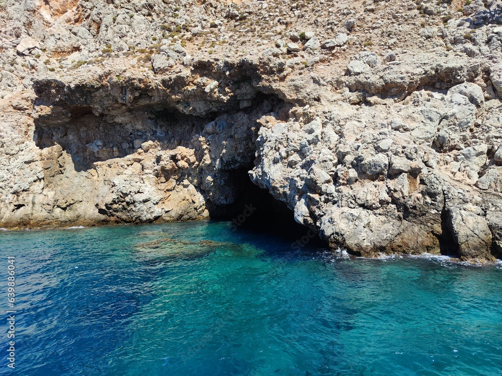 Clear blue sea splashing on grey rock formation in bright sunlight