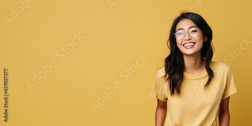 Attractive asian woman wearing yellow tshirt and glasses. Isolated on yellow background.  photo