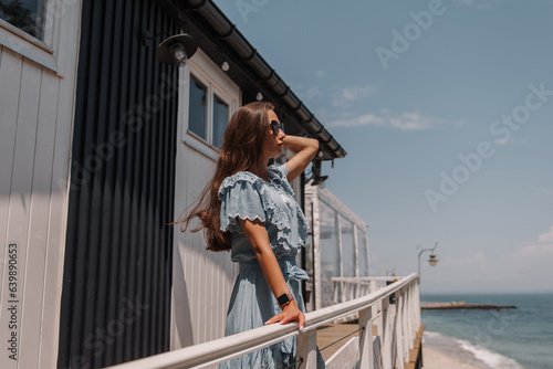 Beautiful young woman in summer dress adjusting hair while relaxing on the sea view terrace