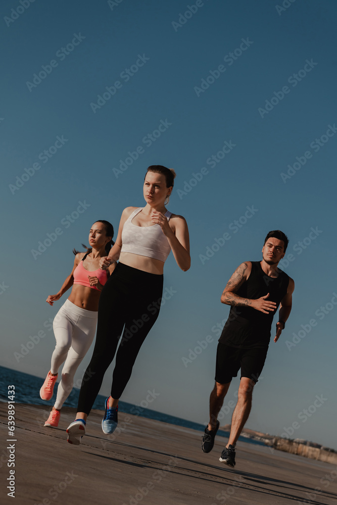 Obraz premium Three confident young people in sportswear looking concentrated while running seaside together