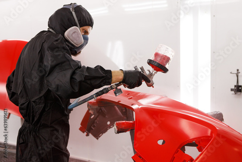 Applying paint to the bumper. Paint the bumper with varnish using an airbrush. Close-up of a spray gun being used by a mechanic while painting a car bumper in a spray booth