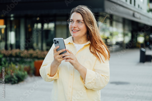 Young happy businesswoman smiling and using smart phone at the city. Beautiful woman on the way to the office searching information on the internet with smartphone. Business  education concept