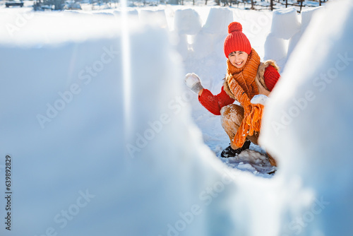 Happy child playing with snowballs in a snow castle. Active winter outdoor games.