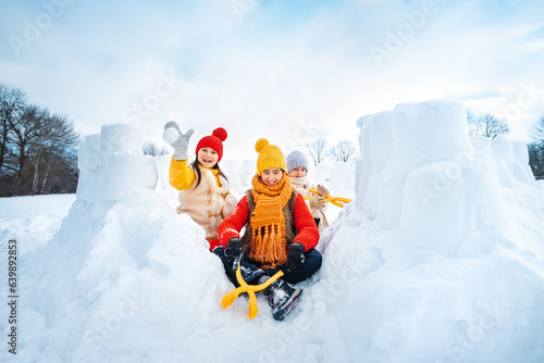 Group of children make snowballs for snowball fights. Children play in snow fort made of ice blocks. Active winter outdoor games.