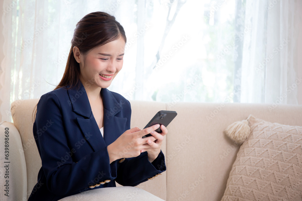 Young asian businesswoman using smartphone to social media online sitting on sofa in living room at home, business woman looking smart phone chat message on couch with confident, lifestyles concept. Young asian businesswoman using smartphone to social media online sitting on sofa in living room at home, business woman looking smart phone chat message on couch with confident, lifestyles concept.