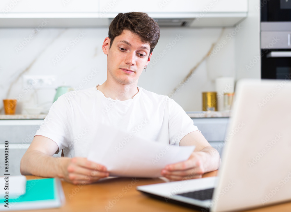 Upset man with laptop and utility bills in kitchen