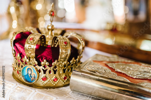 Wedding crown stand on the table in church. Holy Bible decorated with gold icons. Wedding ceremony. Closeup. Divine Liturgy. © Serhii