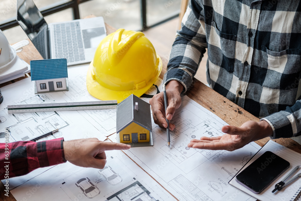 A group of engineers working through blueprints and model houses on their desks. A group of engineers working through blueprints and model houses on their desks.