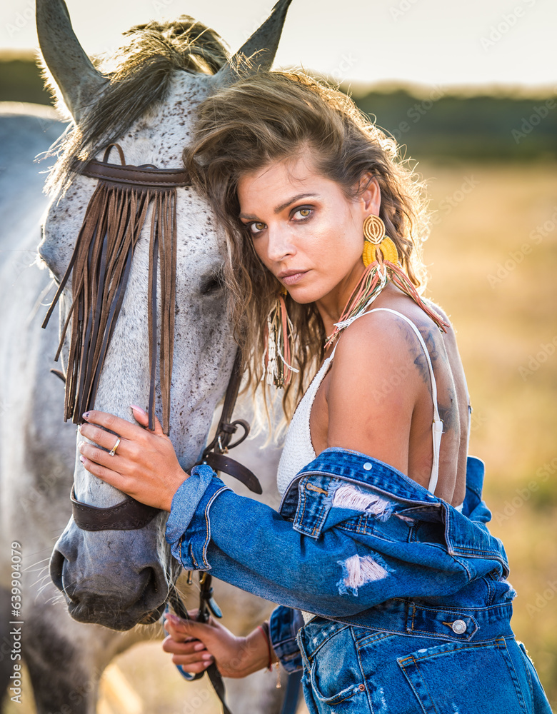 Beautiful blonde woman with curly hair with white hat and horse. Portrait of a girl with denim and her horse. Beautiful girl interacting and having fun with a horse at the ranch