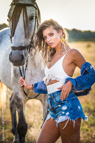 Beautiful blonde woman with curly hair with white hat and horse. Portrait of a girl with denim and her horse. Beautiful girl interacting and having fun with a horse at the ranch