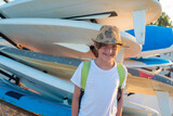 smiling child in a t-shirt with a backpack at the surf station on the beach in summer. joyful 10 year old child stands next to the windsurf boards, waiting for a workout.