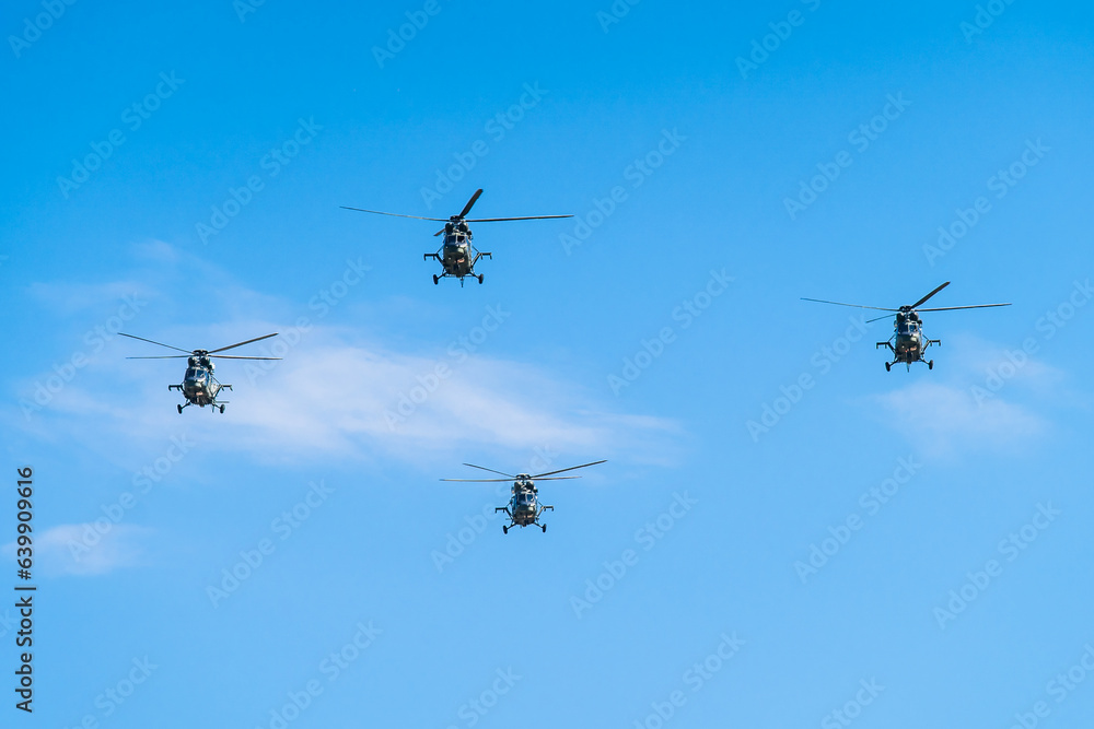 Four helicopters flying in formation against a clear blue sky