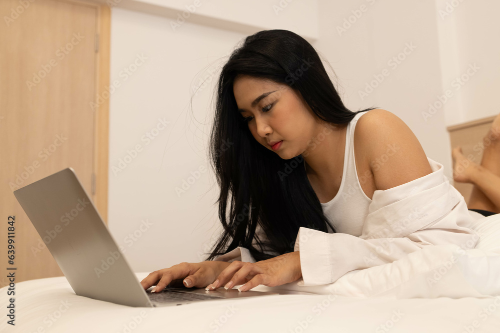 A casual beautiful woman working on a laptop lying on the bed in a hotel, or house A casual beautiful woman working on a laptop lying on the bed in a hotel, or house
