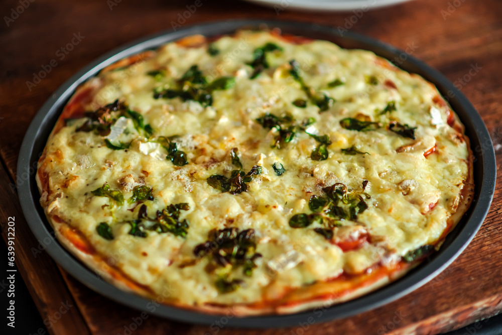 Freshly cooked pizza with lots of cheese and greens in a round shape on a wooden background. Freshly cooked pizza with lots of cheese and greens in a round shape on a wooden background.