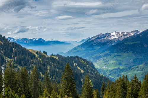 Spring sunlight illuminating the forests, farms and the partially snow-covered mountains of the Großes Walsertal in the Austrian Alps, Vorarlberg, with mist covering the valley in the background