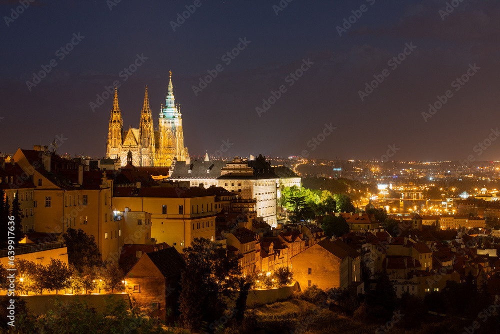 Night time view towards Prague Castle and St. Vitus Cathedral lit up on the hilltop as well as the lights of the historical Old Town next to the Vltava River in the valley
