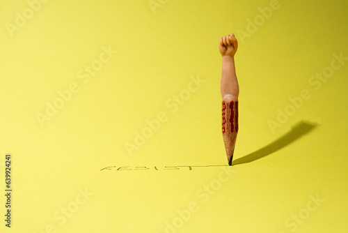 Fotografia Surreal abstract scene with an old wooden pencil from where comes out a human hand with a fist symbolizing strenght, power, resistance