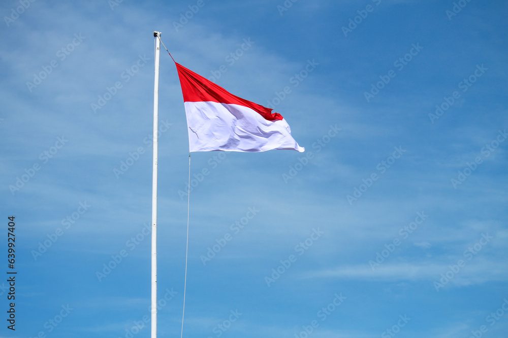 The Indonesian flag flutters on a bamboo pole against a blue sky background, waving the red and white flag The Indonesian flag flutters on a bamboo pole against a blue sky background, waving the red and white flag