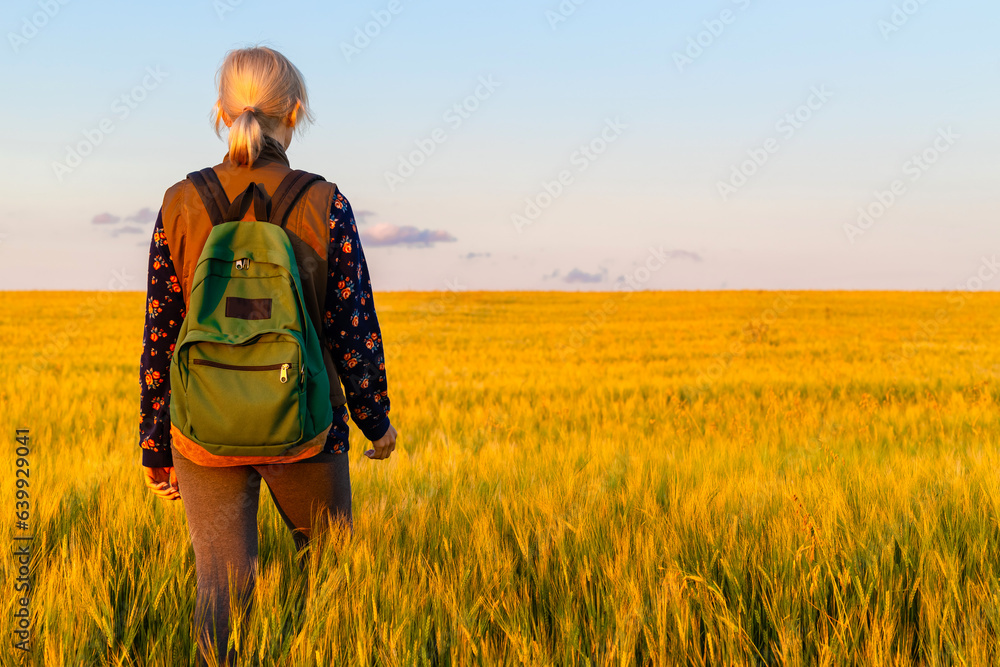 Ryazan, Russia - July 20, 2023: a girl with a backpack walks through a field with young wheat. tourist walks through the field Ryazan, Russia - July 20, 2023: a girl with a backpack walks through a field with young wheat. tourist walks through the field