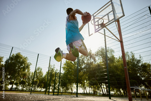 Teenager player throwing ball into basketball hoop, shot in motion, bottom view