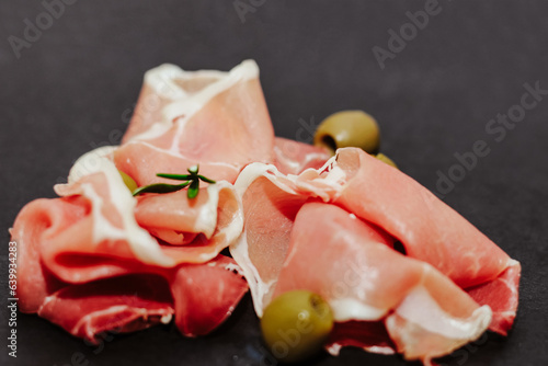 Pieces of dried pork jamon prosciutto with olives on a black board.
