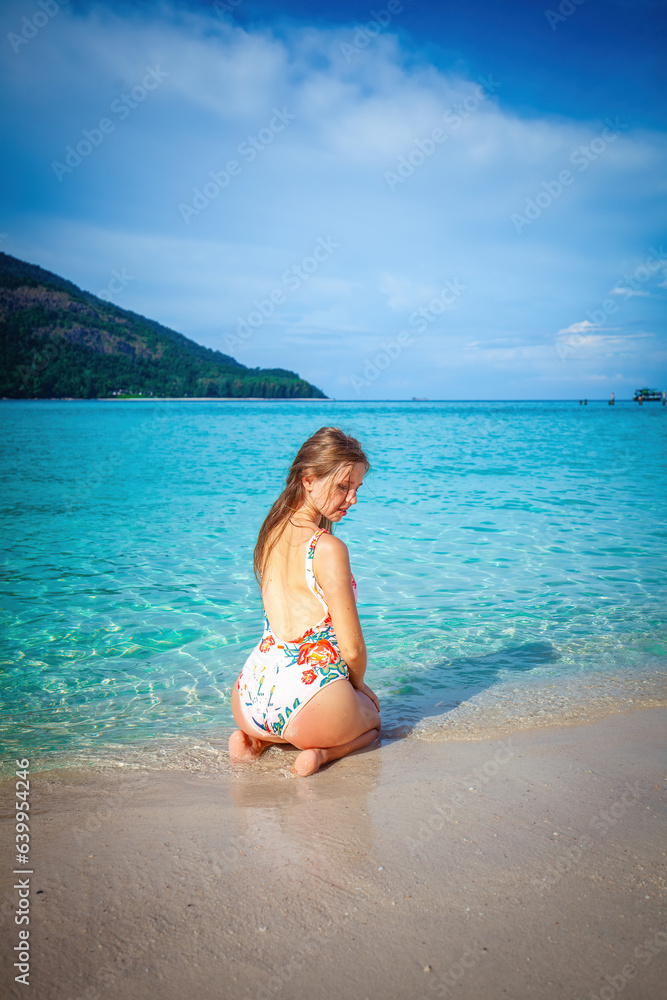 Slim woman in swimwear enjoys the hot summer day, reclining on the beach with a stunning turquoise backdrop. Concept of beach vacation and natural beauty.