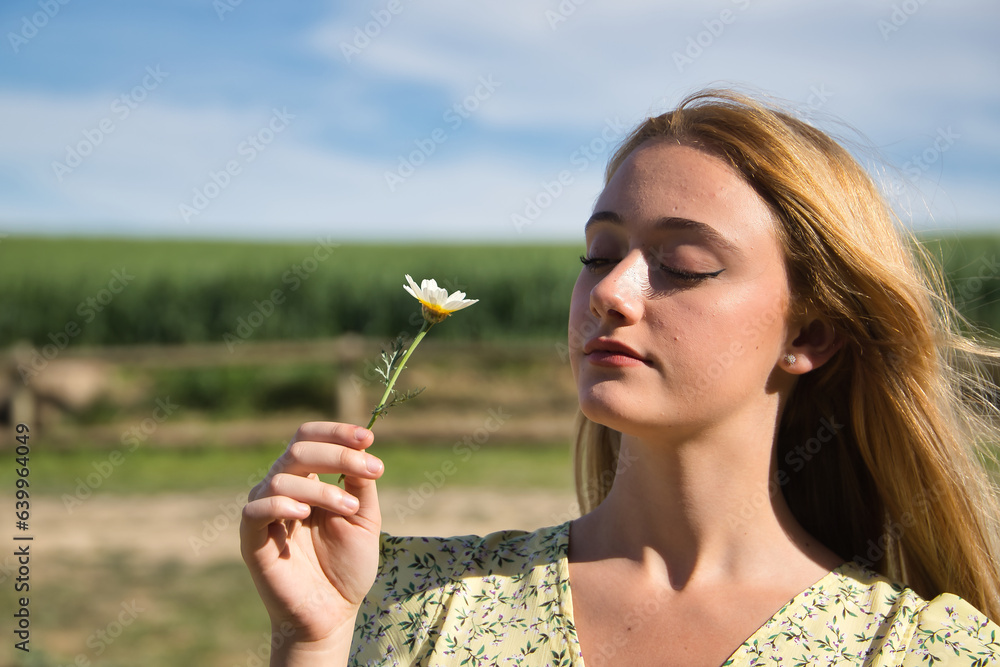Young woman, beautiful and blonde in a yellow dress, watching a daisy in the middle of the field, calm and relaxed. Concept spring, flowers, peace, fields, meadows. Young woman, beautiful and blonde in a yellow dress, watching a daisy in the middle of the field, calm and relaxed. Concept spring, flowers, peace, fields, meadows.