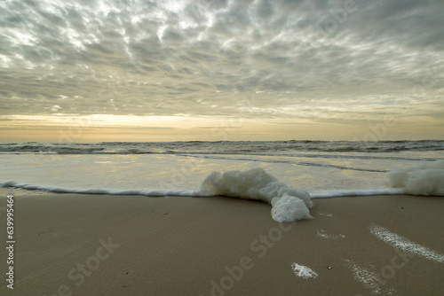 windy beach, sea foam and low clouds at sunset