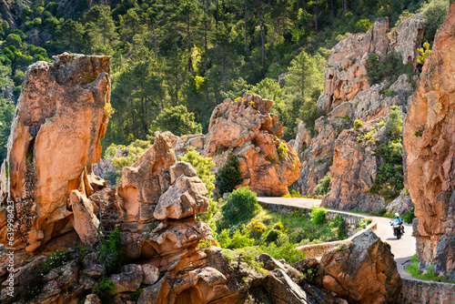 Motobiker on road among the rocks of Calanche de Piana, Les Calanques de Piana in Corsica, France