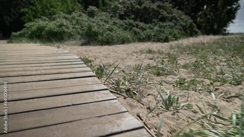 The camera moves along a wooden deck among the sand in a coastal park, simulating the movement of a person or vehicle. Close-up.