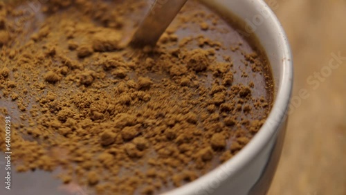 Morning cup of cinnamon black tea. Stirring with a teaspoon of aromatic healthy additive close up on a wooden table