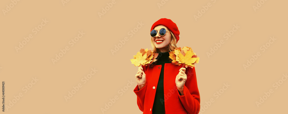 Autumn color style outfit, portrait of beautiful smiling young woman with yellow maple leaves wearing red french beret hat, coat on brown studio background