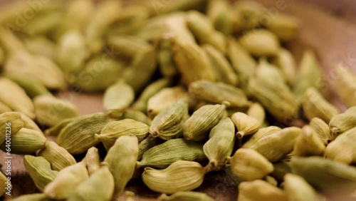 Hand takes handful of cardamom seeds or cardamon pods from wood rustic bowl. Macro. Slow motion