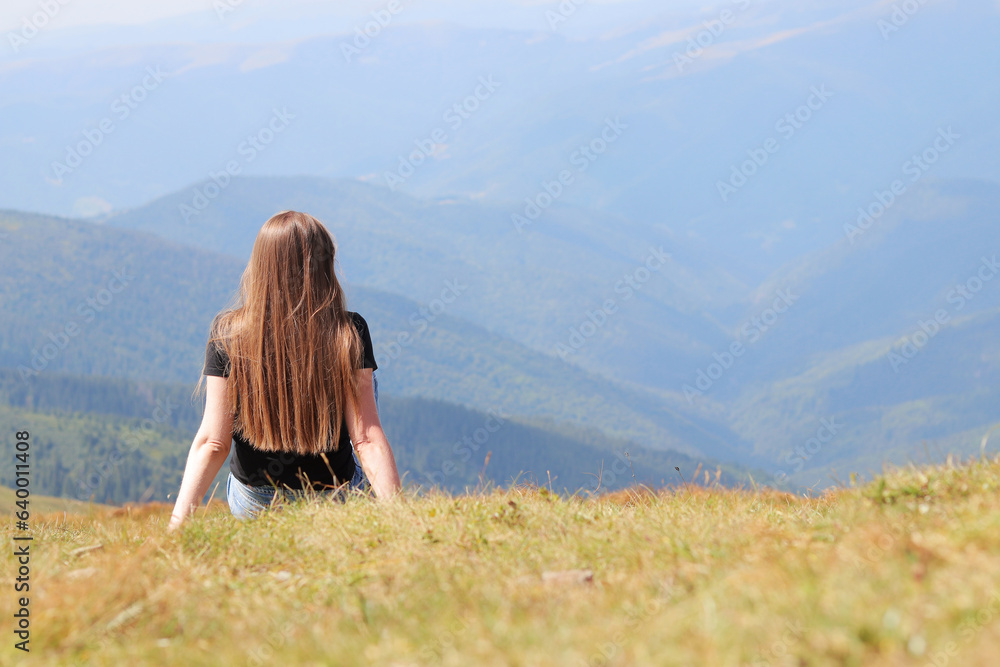 The concept of relaxation, tourism and recreation. A trip to the Carpathians, Ukraine. View from the back of a girl sitting on the grass in front of a mountain landscape, nature