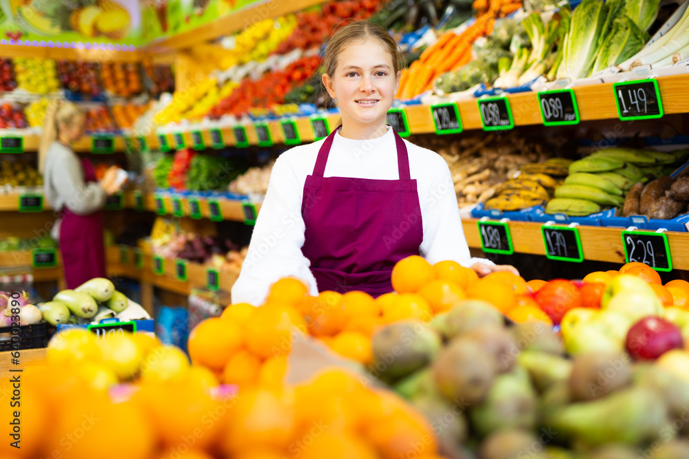 Portrait of smiling young girl wearing apron standing in fruit and vegetable store. First job concept..