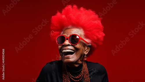 Happy, laughing, lovely old woman, with red afro hair and red sunglasses, on solid colour background, with room for text.