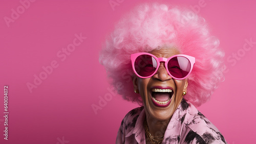 Happy, laughing, lovely old woman, with pink afro hair and pink sunglasses, on solid colour background, with room for text.