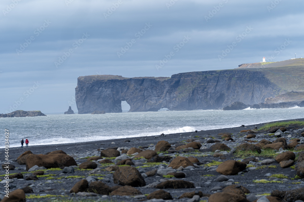 Black sand beach looking toward sea stacks and arches, in Vik, Iceland, Dyrholaey. Unidentifiable people for scale