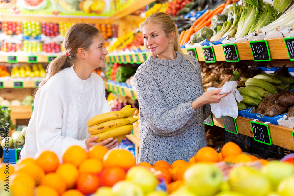 Portrait of teenage girl and her mother who buying fresh vegetables and ...