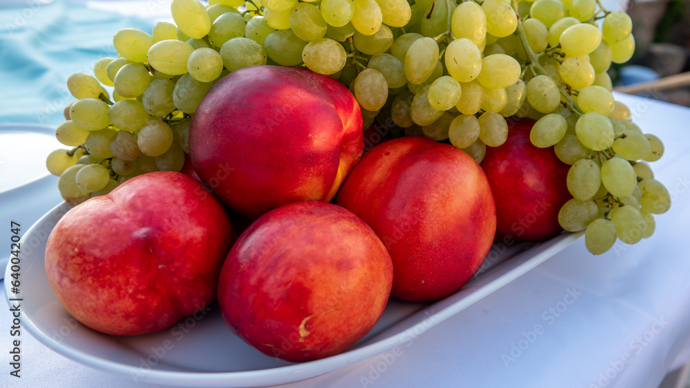 delicious green grapes and red peaches on a large porcelain plate on a restaurant table