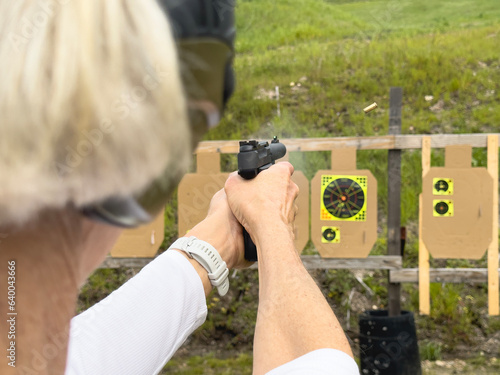A female aiming a 9mm handgun at a practice target. A bullet cartridge is seen exiting the gun with a little bit of smoke. photo