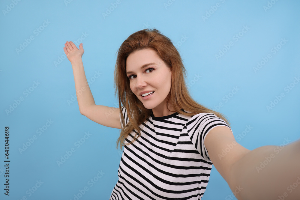 Fototapeta premium Beautiful woman taking selfie on light blue background
